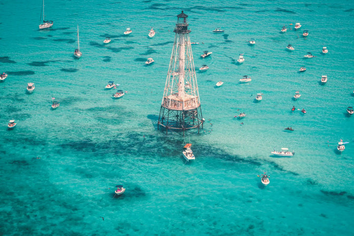 Lighthouse surrounded by boats in clear blue water