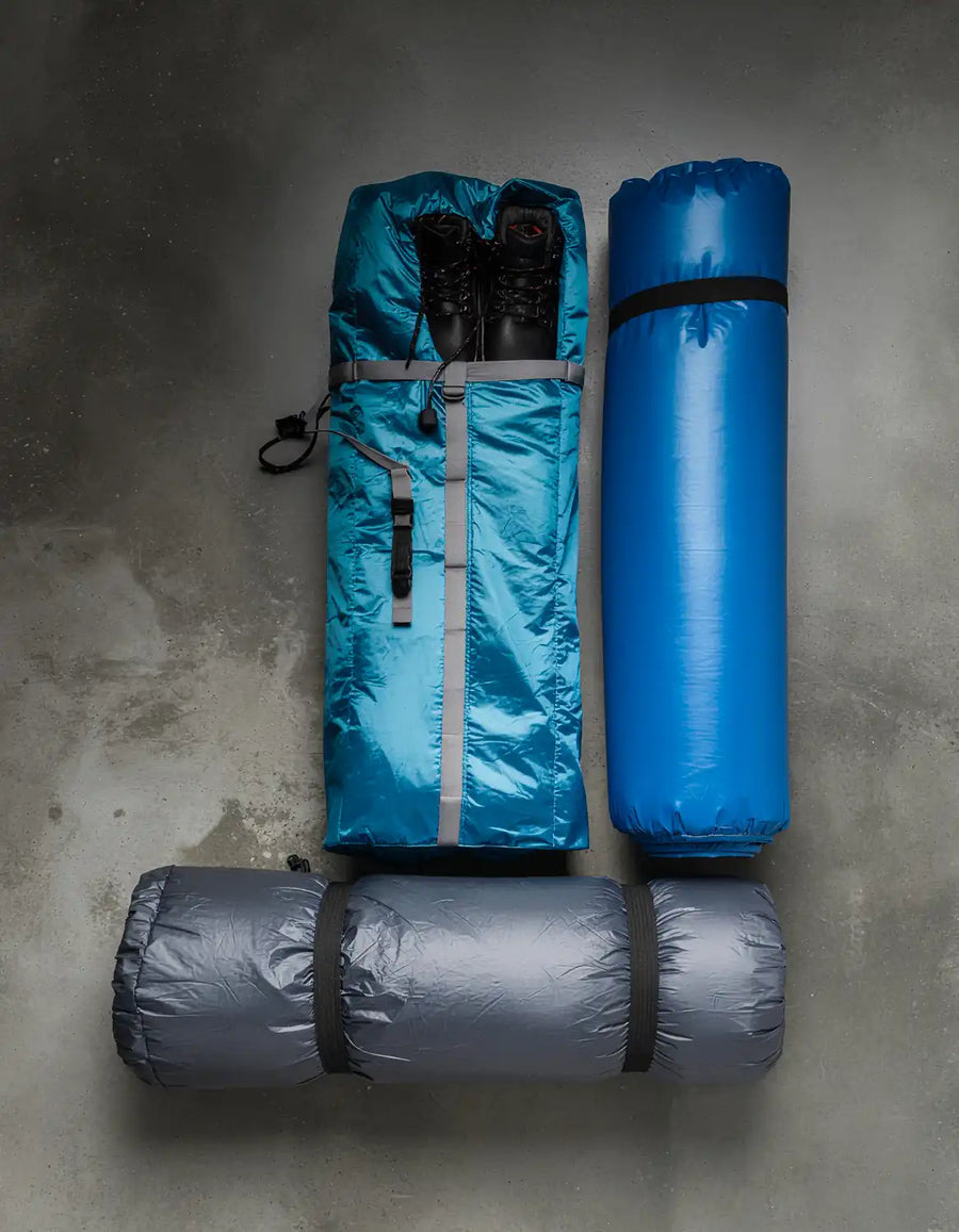 Three rolled-up sleeping bags in blue, gray, and black on a concrete floor.
